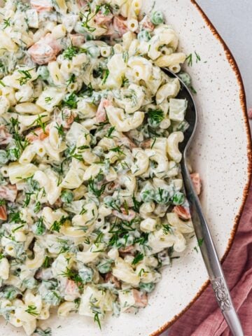 Vegetarian macaroni salad with yogurt, mayonnaise, peas, carrots, fresh dill, potatoes in a ceramic bowl