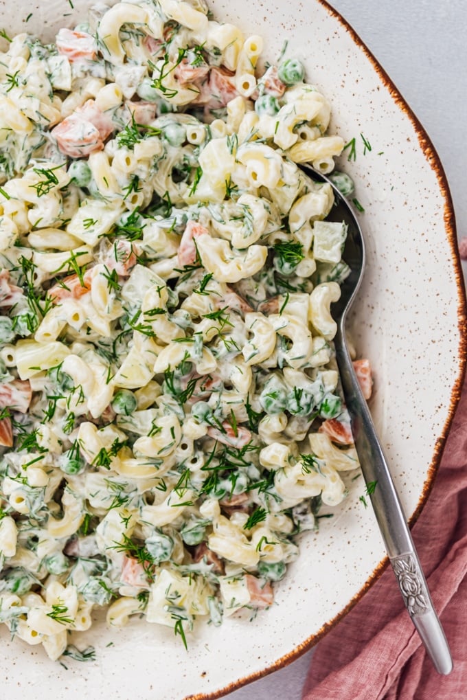 Classic macaroni salad with yogurt, mayonnaise, peas, carrots, fresh dill, potatoes in a ceramic bowl