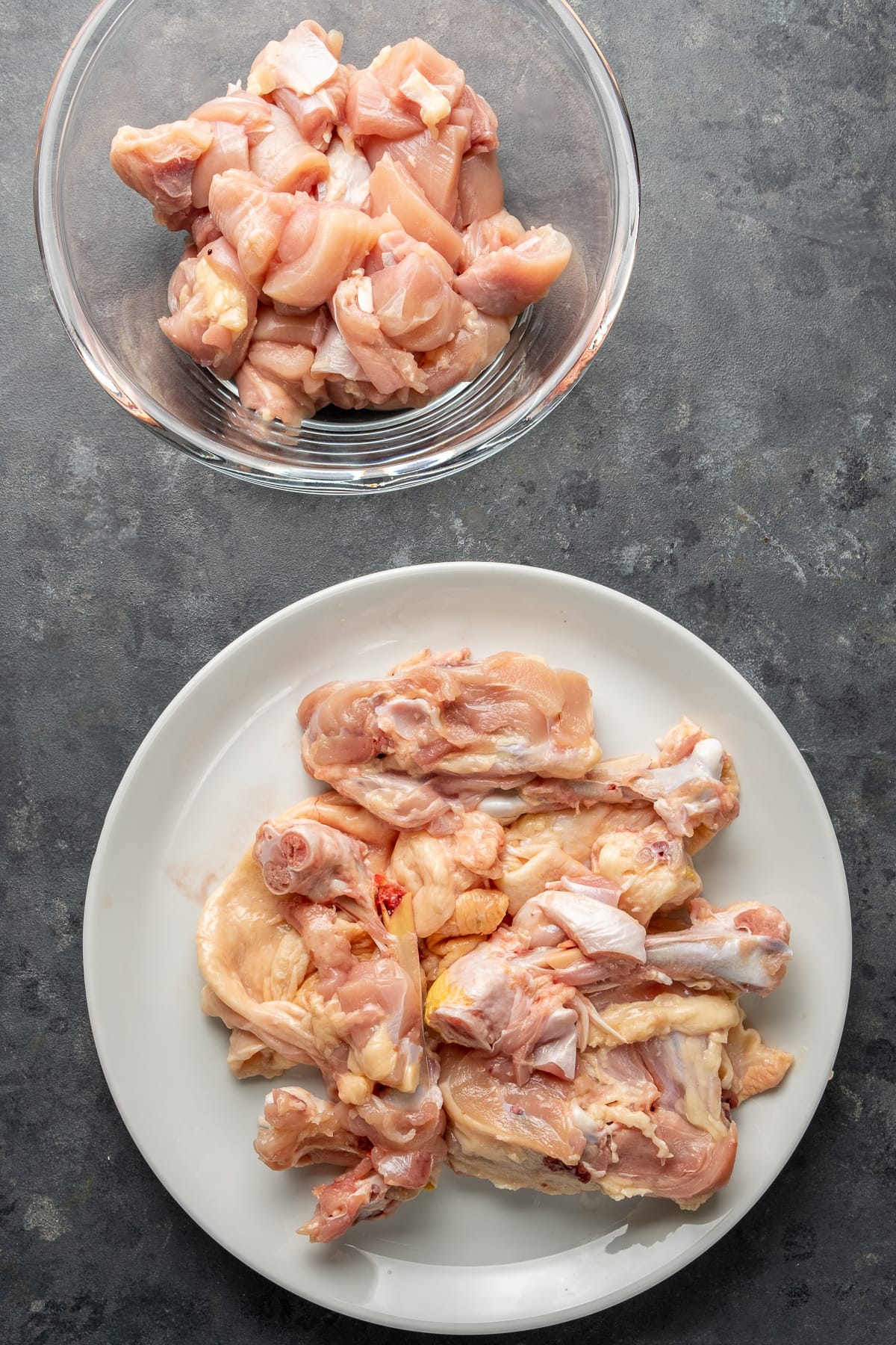 Chicken bones removed on a white plate, diced chicken meat in a glass bowl on a dark background.