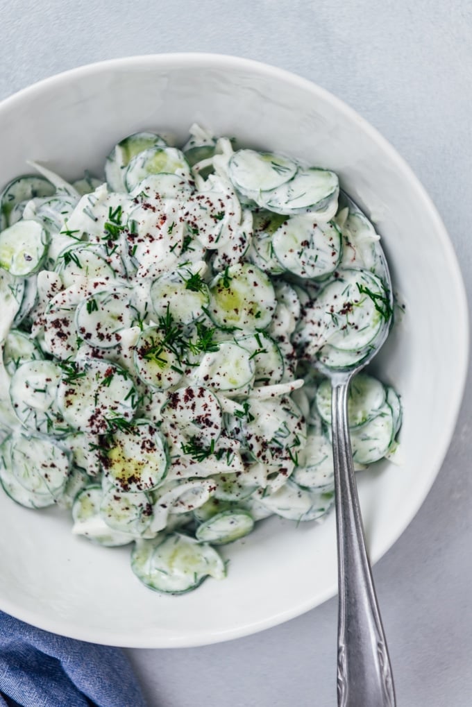 The BEST Creamy Cucumber Salad with onions and yogurt dressing. No mayonnaise. This will be your new summer hit! #creamycucumbersalad #cucumbersalad #saladwithoutmayo #creamycucumbers Creamy cucumber salad with a yogurt and sumac dressing in a white salad bowl
