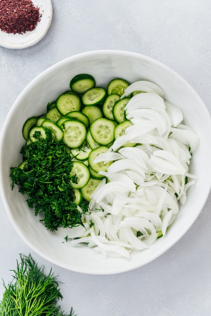 Making the best cucumber salad with onions, dill and yogurt in a white bowl