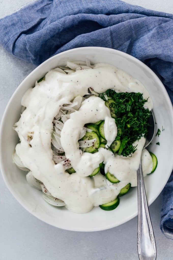 Creamy cucumbers and onions with dill and Greek yogurt in a white bowl