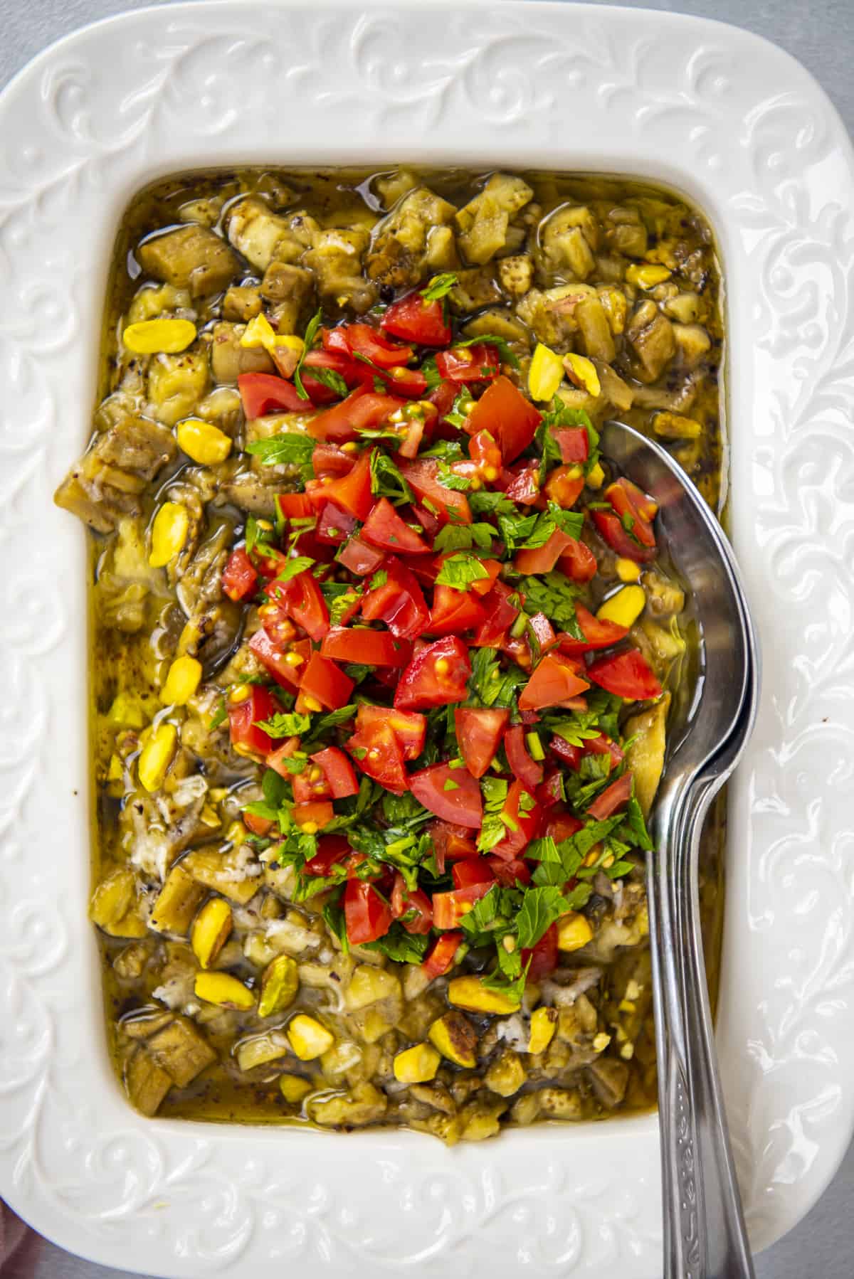 Roasted eggplant salad topped with chopped fresh tomatoes in a white rectangular bowl.