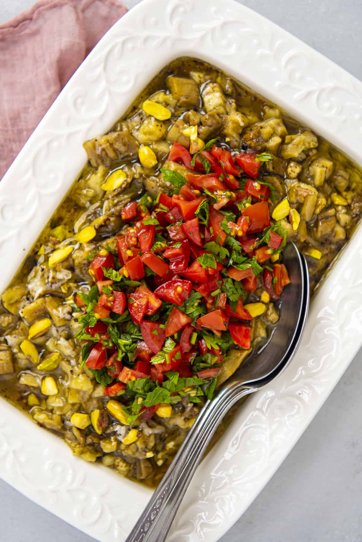 Roasted eggplant salad with tomatoes in a white rectangular baking dish and two spoons in it.