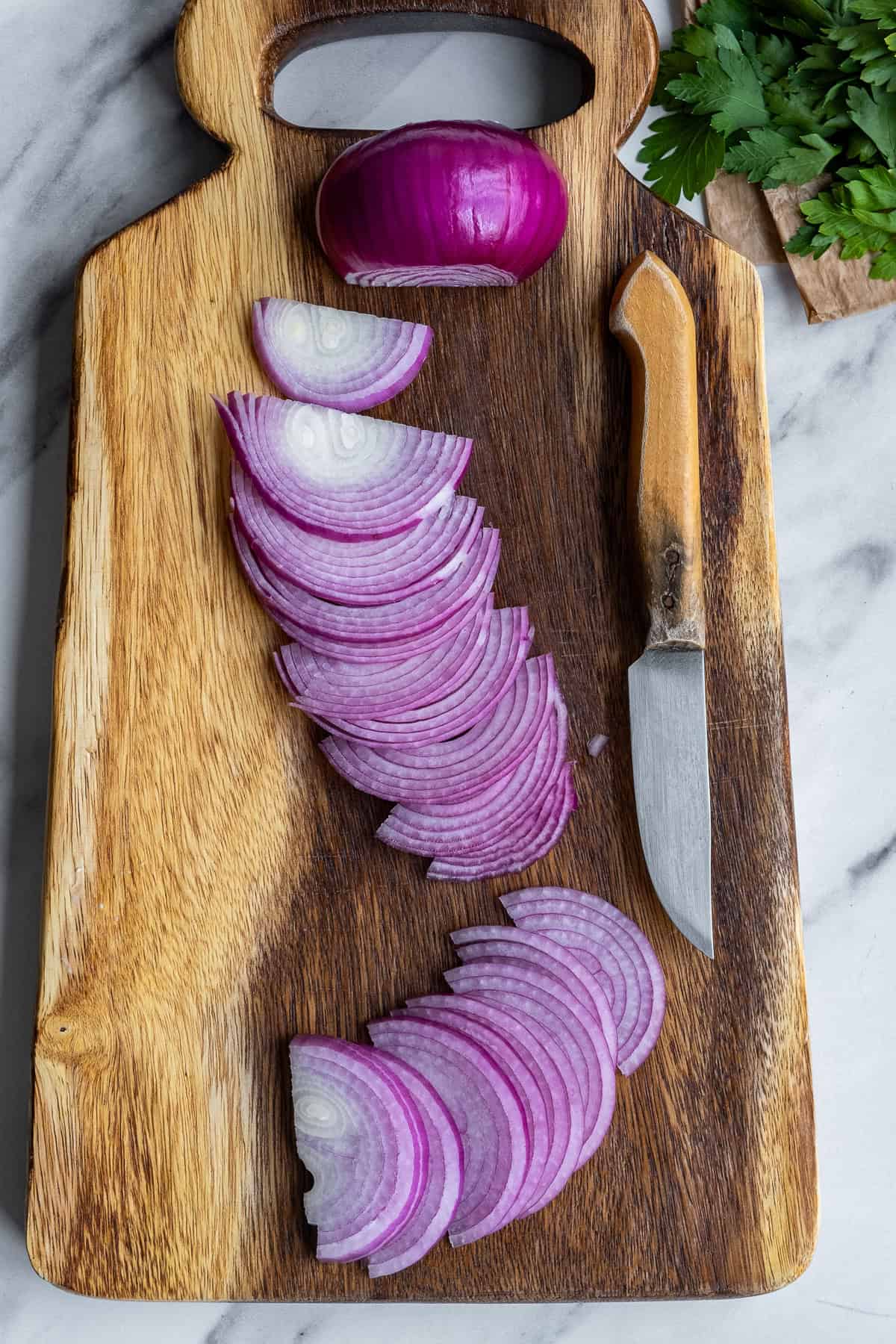 Red onions sliced on a wooden cutting board and a knife accompanies.