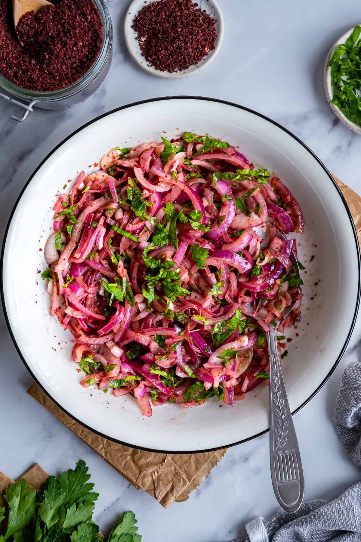 Turkish sumac onions made with red onions, parsley and sumac in a white serving bowl.