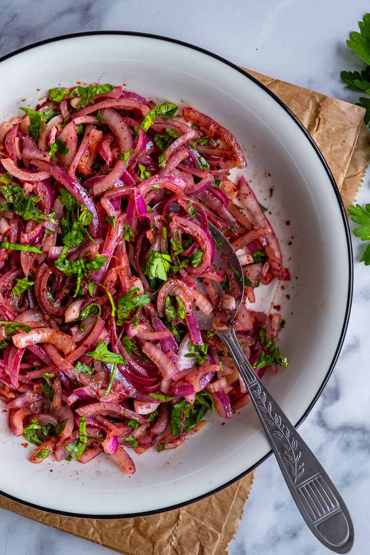 Close-up of Turkish sumac onions made with red onions, parsley and sumac in a white bowl.