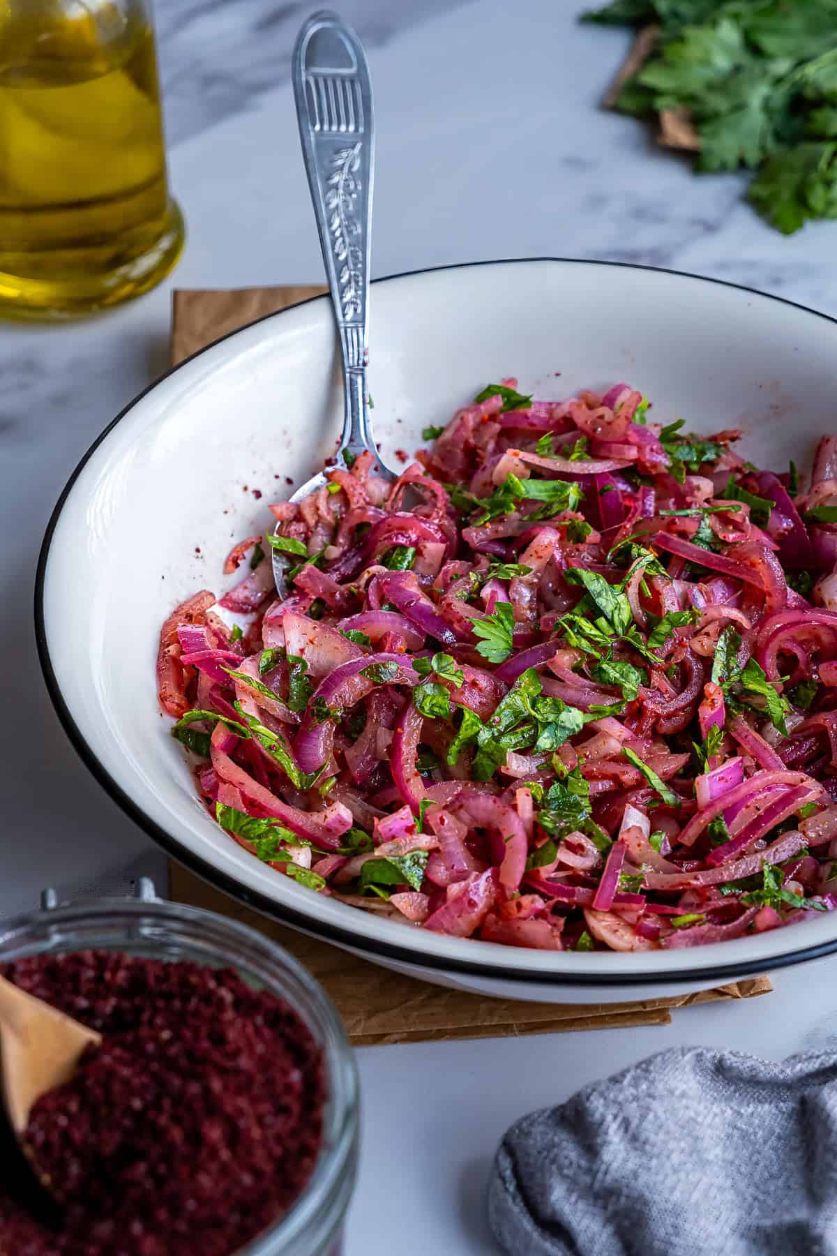 Close-up of Turkish sumac onion salad made with red onions, parsley and sumac in a white serving bowl.