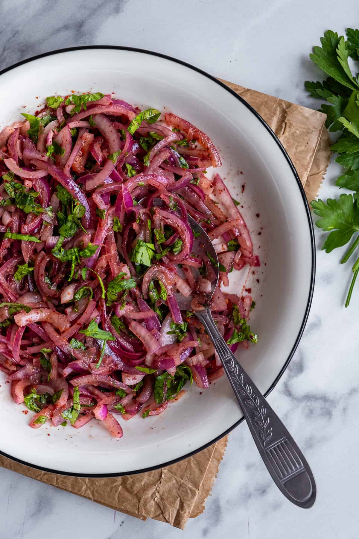 Sumac marinated onions with parsley in a white bowl and a spoon inside it.
