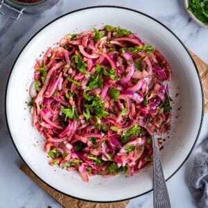 Turkish sumac onion salad made with red onions, parsley and sumac in a white serving bowl.