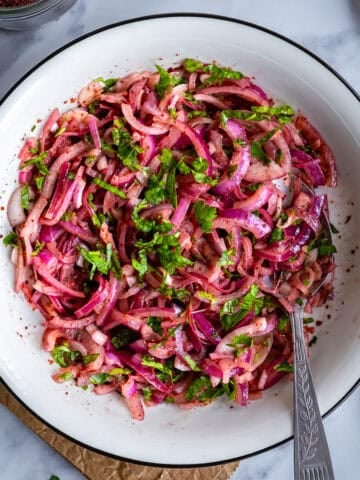 Turkish sumac onion salad made with red onions, parsley and sumac in a white serving bowl.