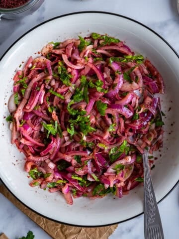 Overhead view of Turkish sumac onion salad made with red onions, parsley and sumac in a white serving bowl.