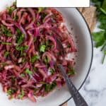 Red onion salad with sumac in a white bowl, fresh parsley on the side.