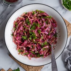 Marinated red onions with sumac in a white bowl and a spoon in it.