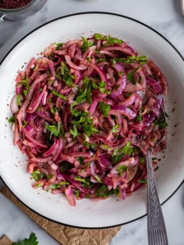 Marinated red onions with sumac in a white bowl and a spoon in it.