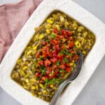 Eggplant salad with tomatoes in a white rectangular dish and two spoons inside it.