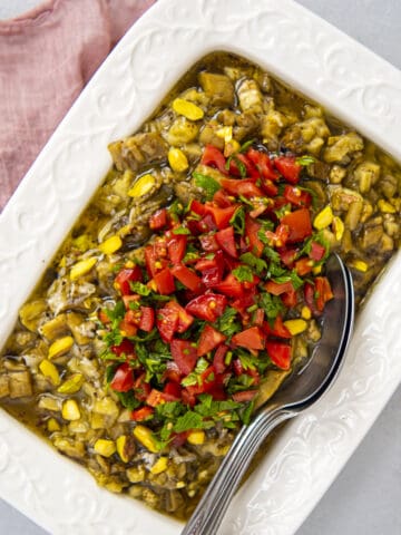 Eggplant salad with tomatoes in a white rectangular dish and two spoons inside it.