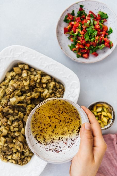 Pouring olive oil and vinegar salad dressing over chopped roasted eggplants