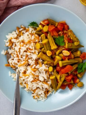 Okra stew served with rice in a blue bowl with a spoon inside it.