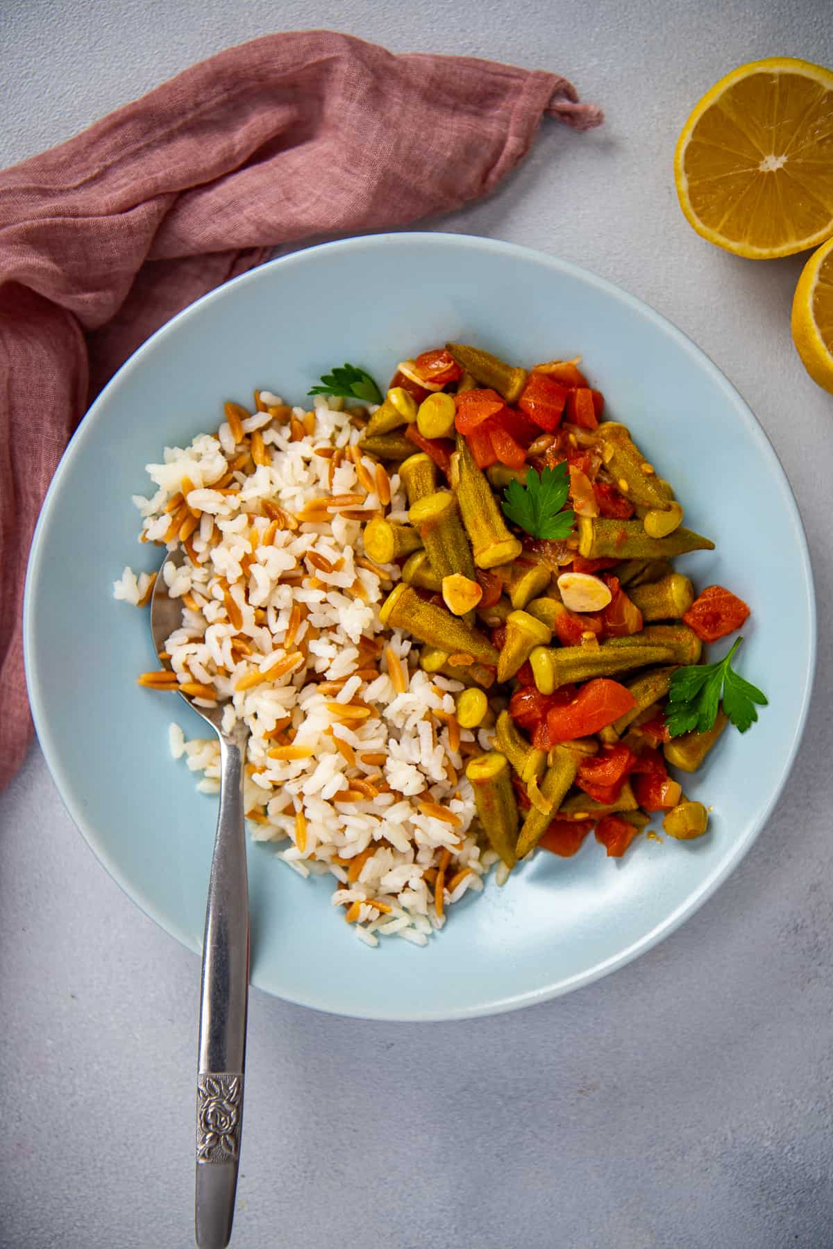 Okra stew served with rice pilav in a blue bowl with a spoon inside it.