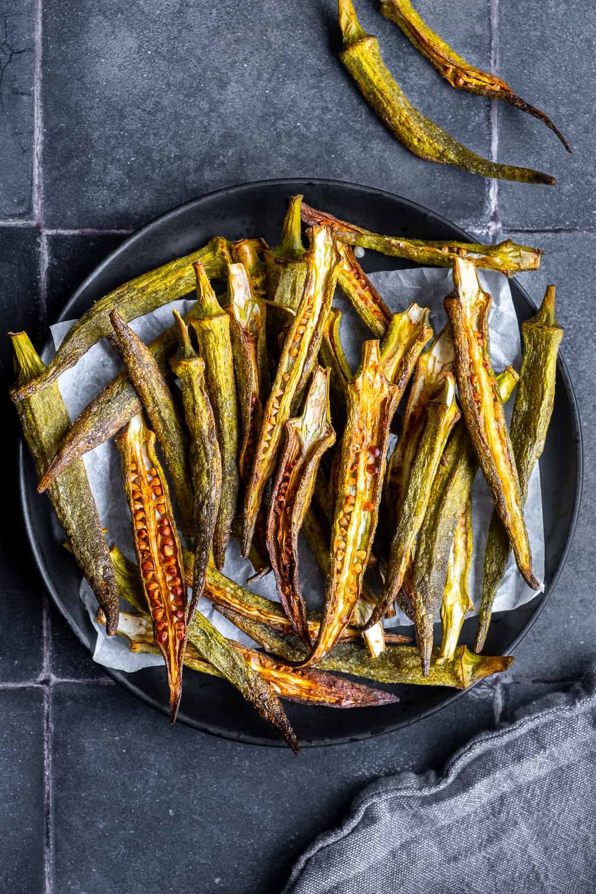 Homemade okra chips on a black plate.