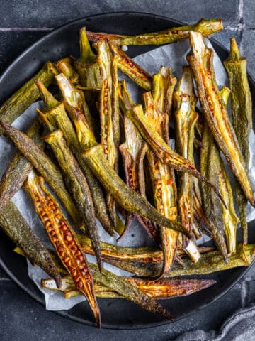 Okra chips on a black plate on grey tiles.