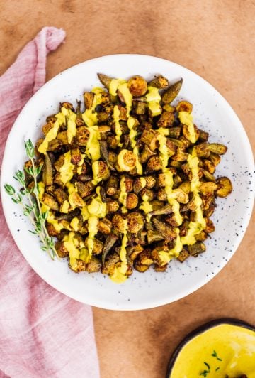 Spicy oven roasted okra drizzled with turmeric tahini sauce in a bowl