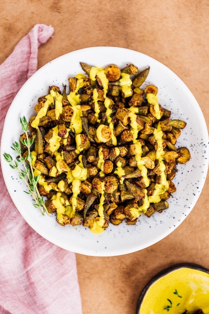 Oven roasted Okra Recipe is for those who hate okra. These crispy roasted okra chips will become their new favorite snack. Healthy and incredibly tasty! #roastedokra #okrarecipe #healthysnack Spicy oven roasted okra drizzled with turmeric tahini sauce in a bowl