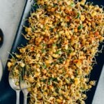 Spicy sprouted lentils with corn served on a black rectangular plate with a spoon and a fork on the side.