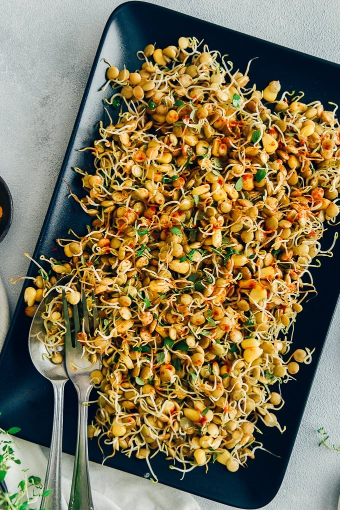 Spicy sprouted lentils with corn served on a black rectangular plate with a spoon and a fork on the side. 