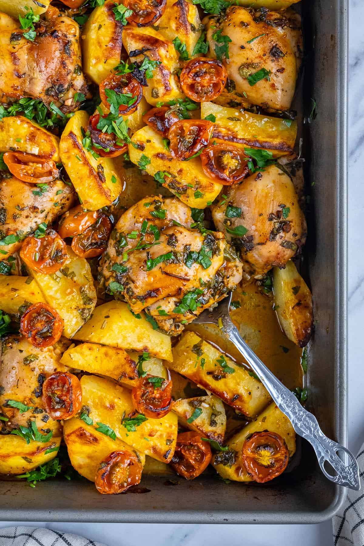 Boneless, skinless chicken thighs baked with potatoes in a baking pan.