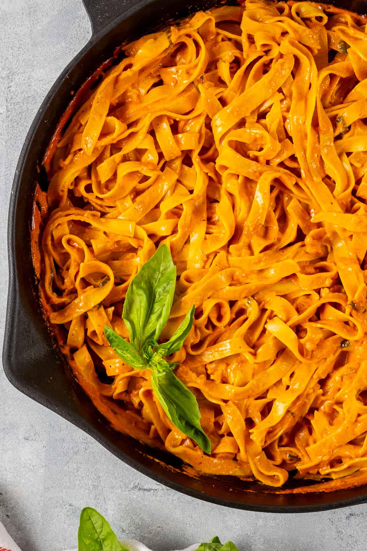 Pasta with creamy tomato sauce garnished with fresh basil in a skillet.