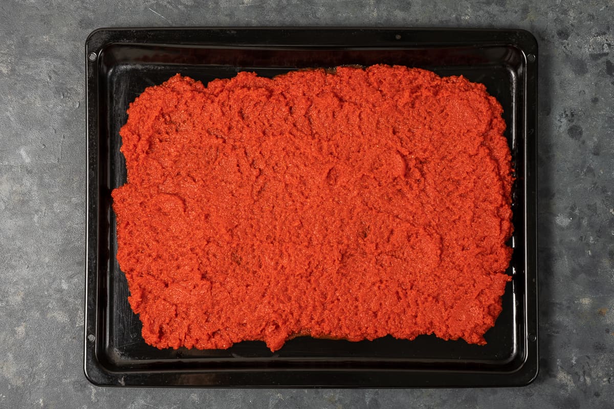 Strained tomato puree on a black baking sheet.