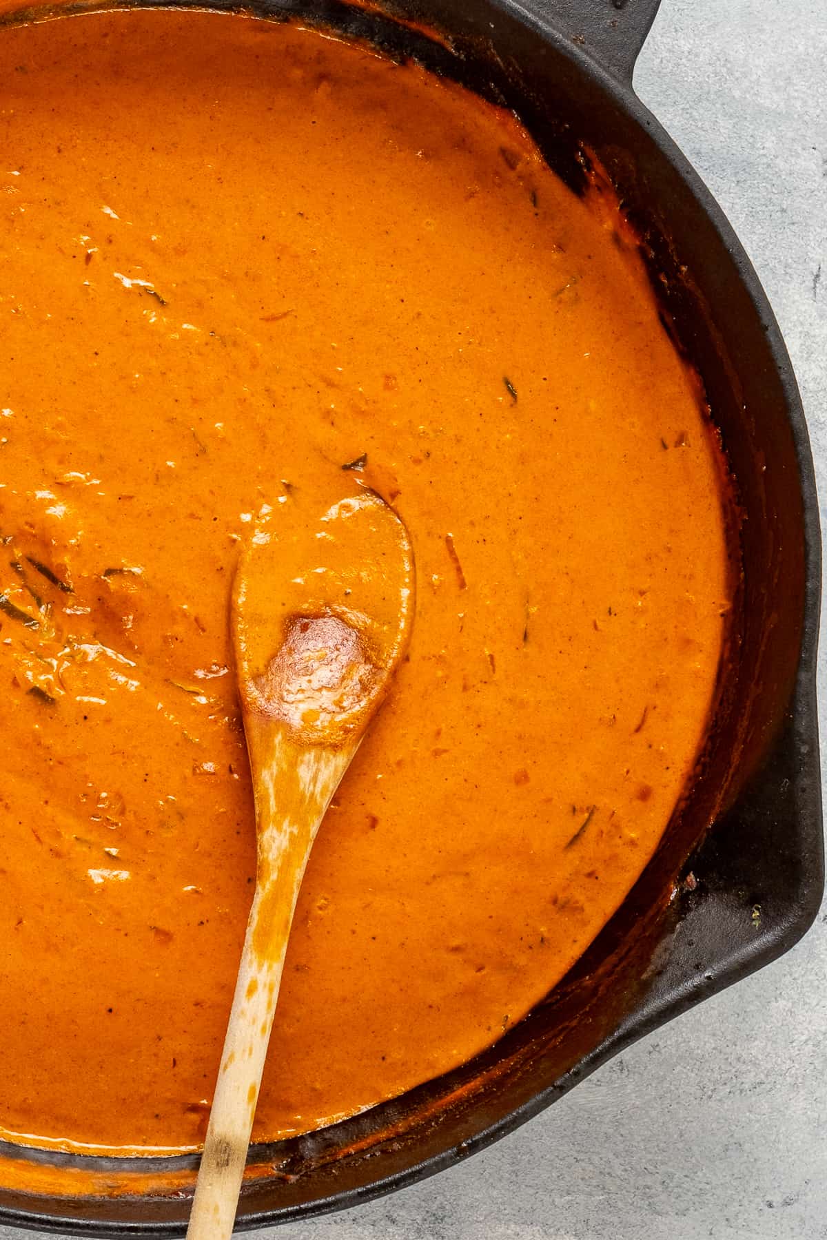 Tomato cream sauce in a skillet and a wooden spoon in it.