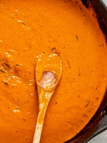 Creamy tomato sauce in a skillet and a wooden spoon inside it.