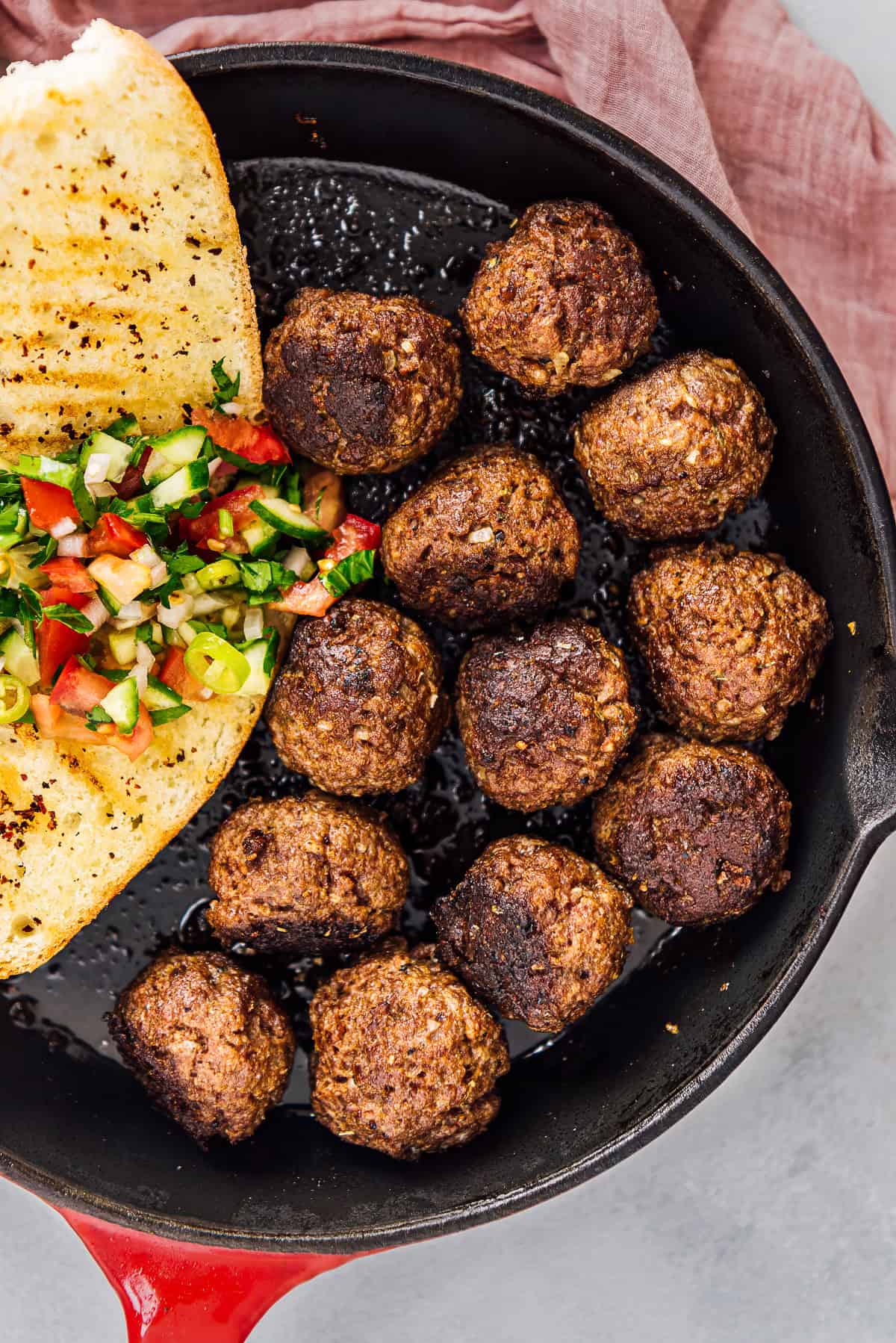 Turkish kofte (meatballs) cooked in a cast iron skillet and served with toasted bread and a fresh chopped salad.