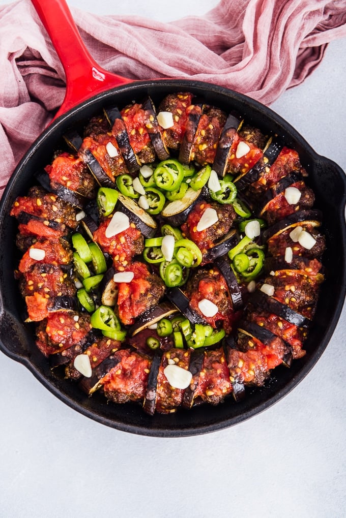 Baked eggplant slices and meatballs topped with tomatoes, green peppers and garlic in a cast iron skillet.