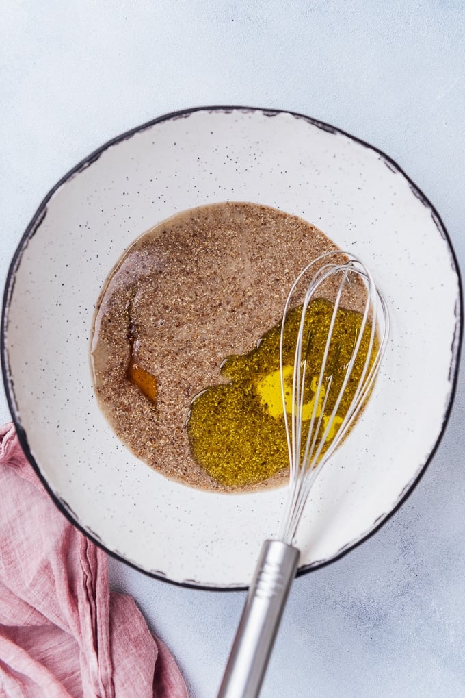 Vegan eggs with ground flax seed in a ceramic bowl with a hand whisk in it.