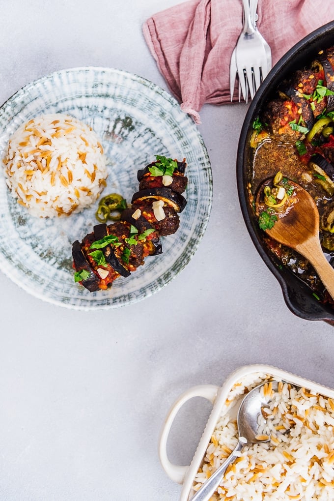 Serving meatball and eggplant kebab casserole with rice pilaf on a ceramic plate.