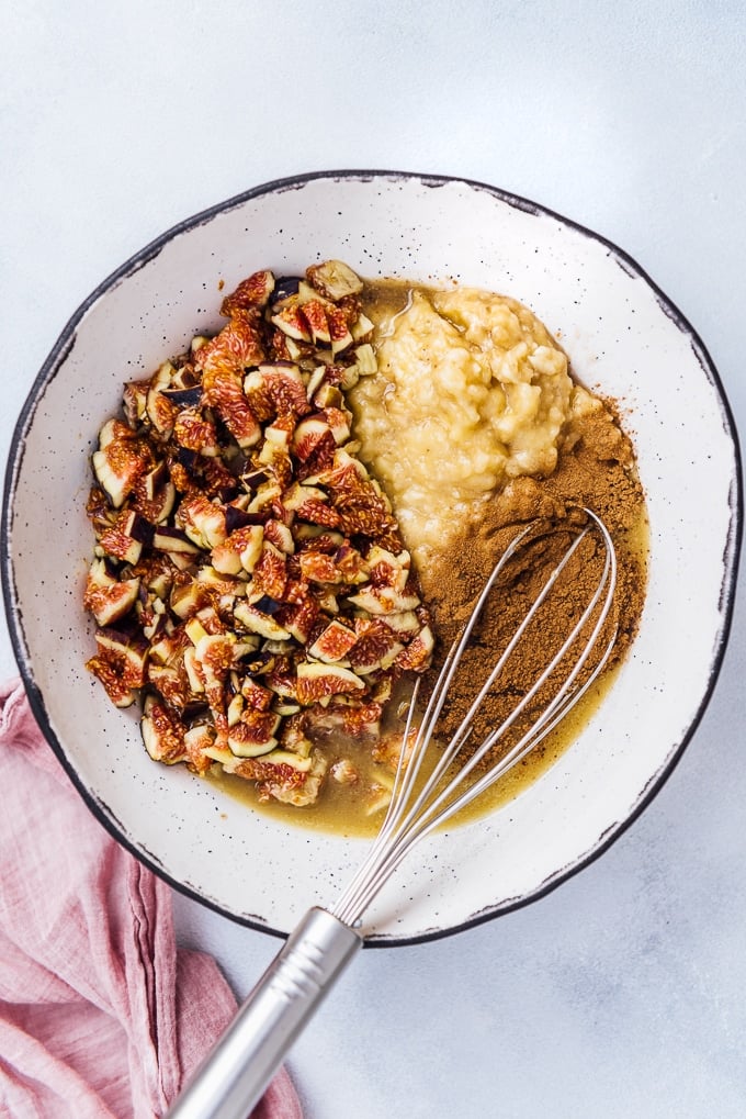 Banana Fig Bread is a PERFECT vegan loaf cake for breakfast. It is sugar free yet so yummy and easy to make. #veganbread #loafcake #figbread #bananabread #sugarfreebaking Fresh figs, mashed banana, cinnamon in a white ceramic bowl with a hand whisk in it.