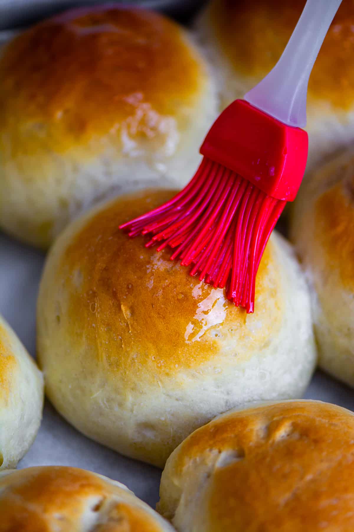 A close shot of a bread roll being brushed with melted butter.