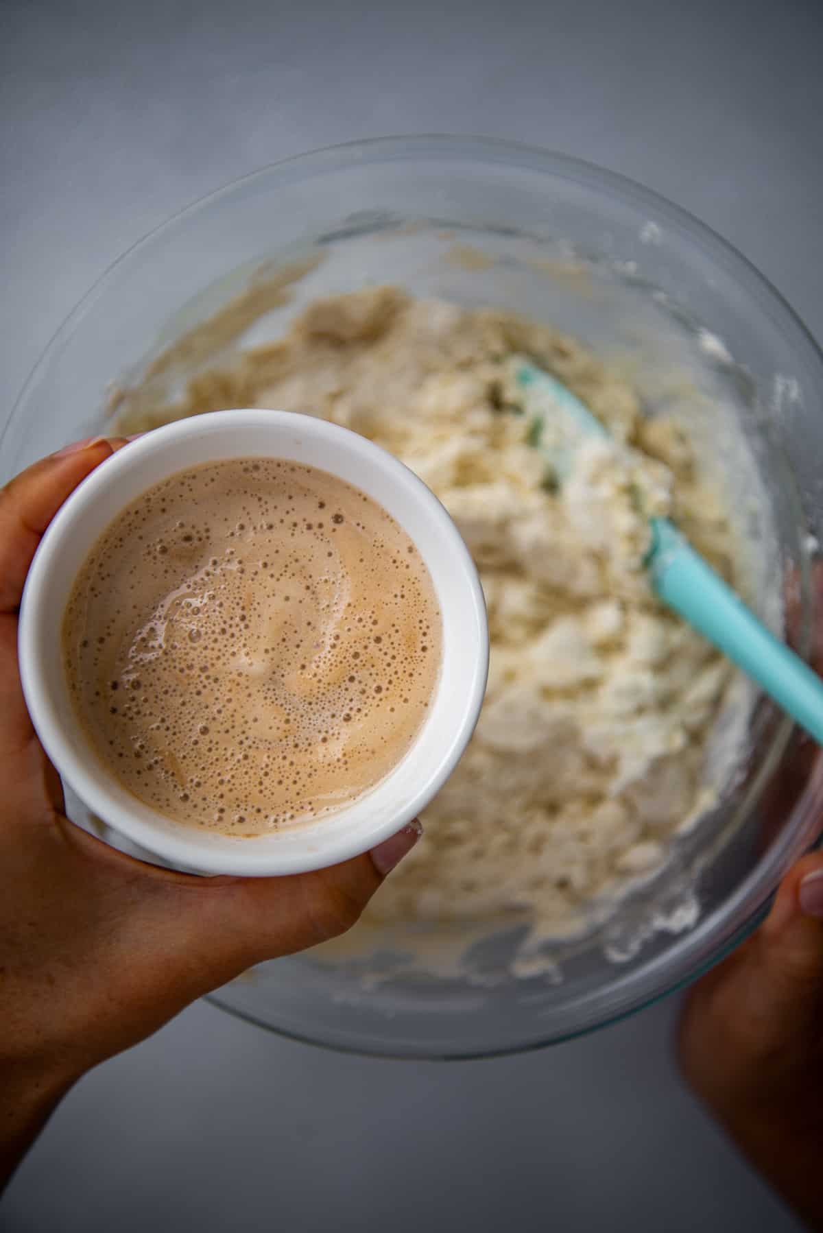 A hand holding a bowl of yeast mixture over the