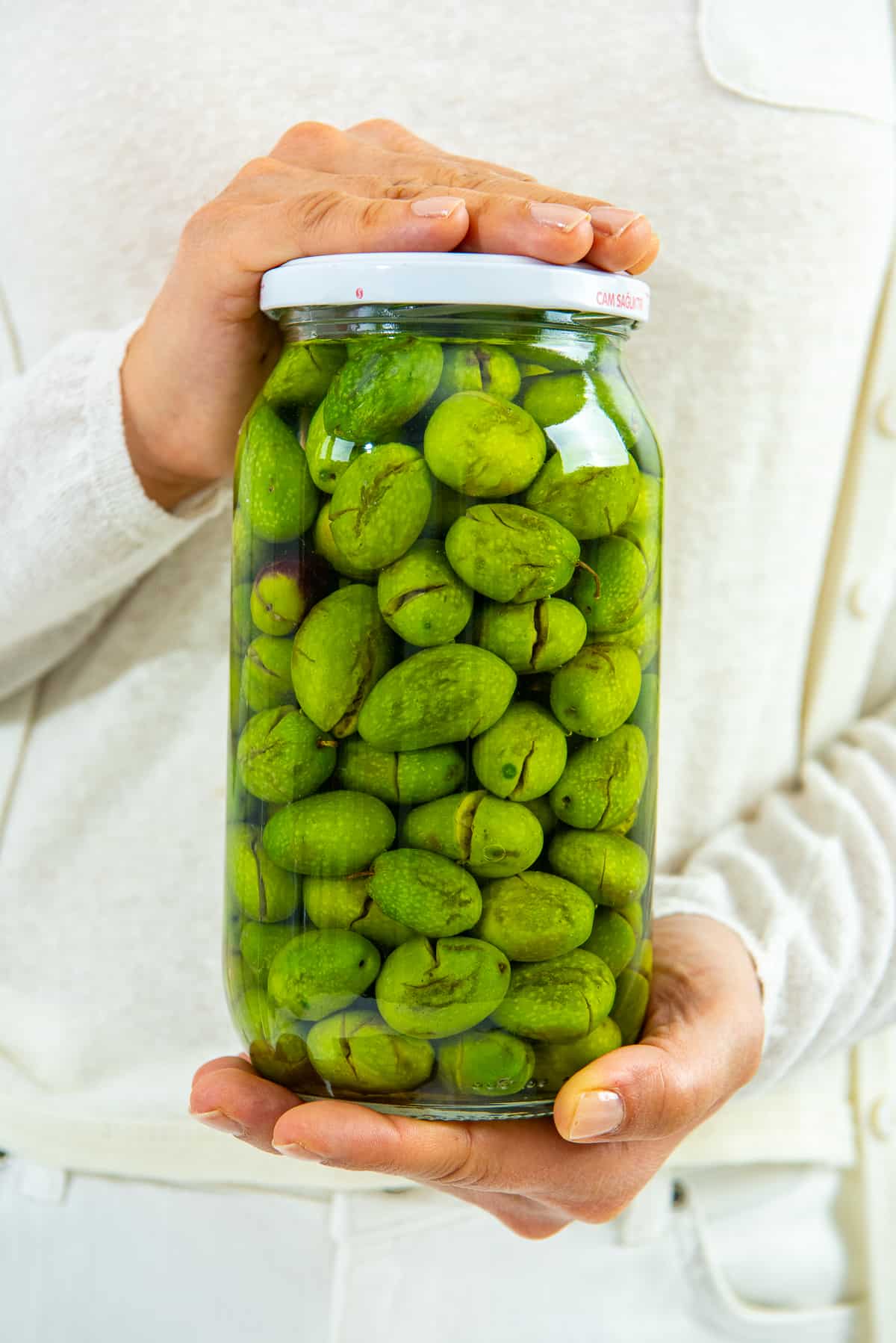 Woman holding a jar of green olives in her two hands.