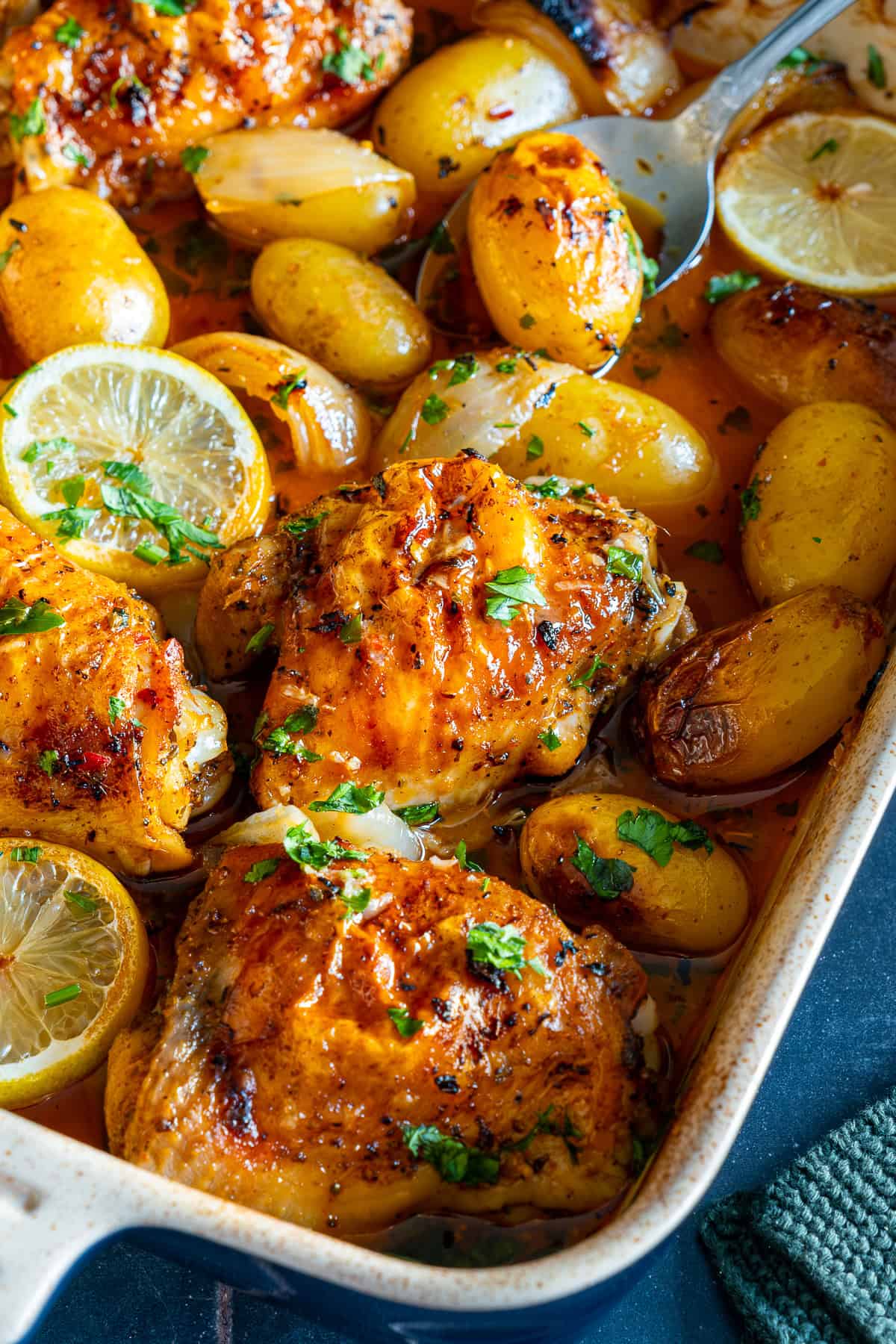 Close-up of golden baked chicken thighs and baby potatoes in a lemon garlic sauce, garnished with parsley and lemon slices.