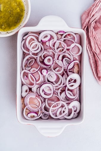 chicken thighs in a casserole pan covered with onion rings