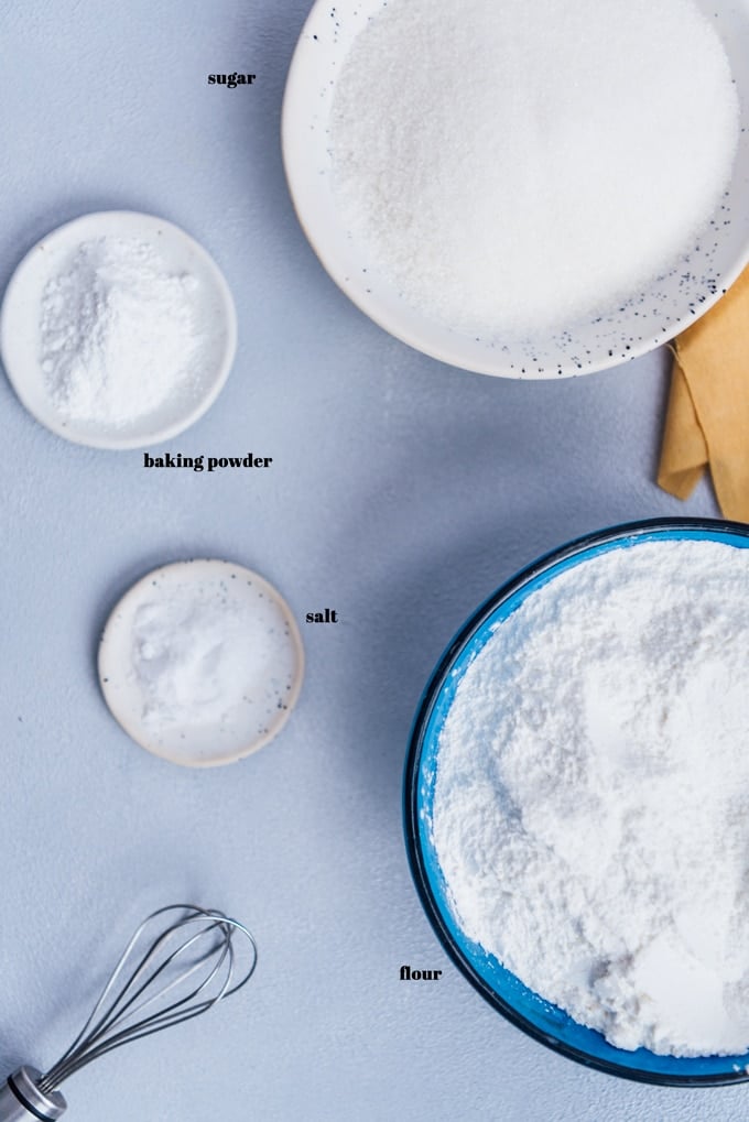 Cake mix from scratch ingredients in ceramiz bowls on a light background and a whisk on the side.