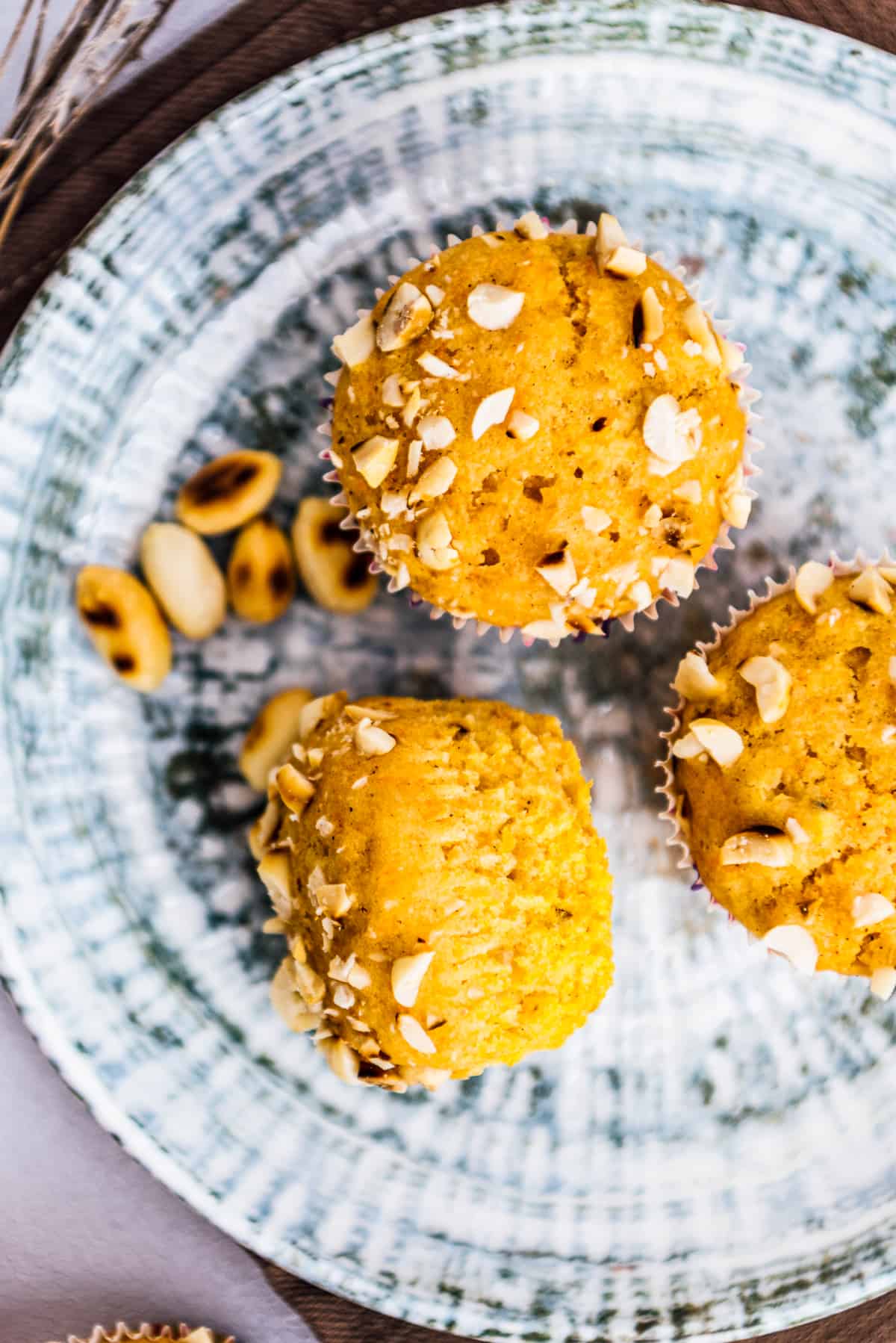 Pumpkin muffins topped with chopped peanuts on a white and grey plate , roasted peanuts on the side.