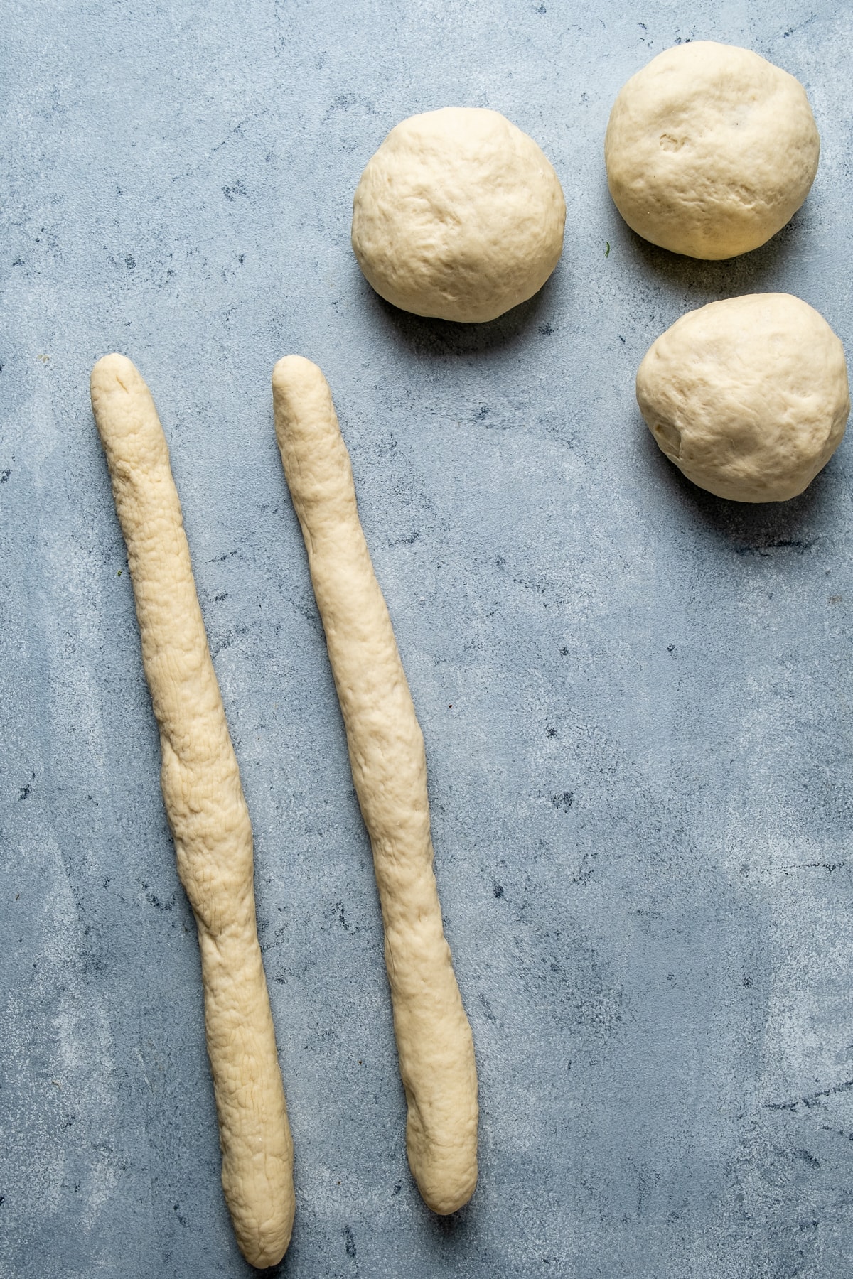 Two strands of dough on a grey background and more dough balls on the side.