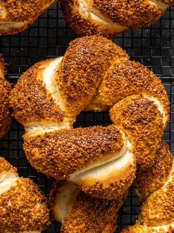 Close shot of a simit bread with a golden color coated with sesame seeds on a dark background.