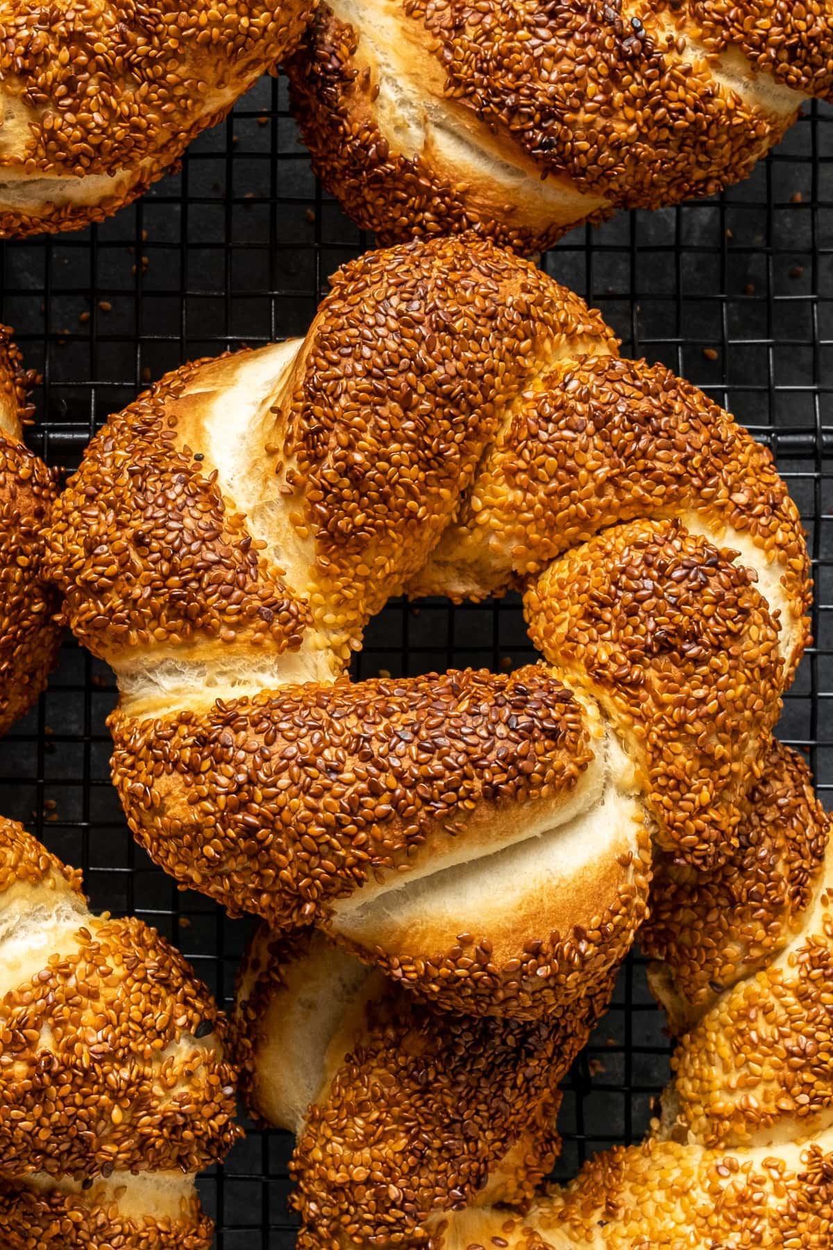 Close shot of a simit bread with a golden color coated with sesame seeds on a dark background.